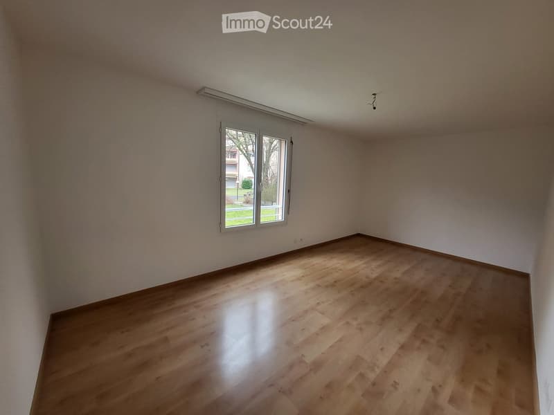 Empty room with wooden flooring and white walls, featuring a large window with white frame and blinds.