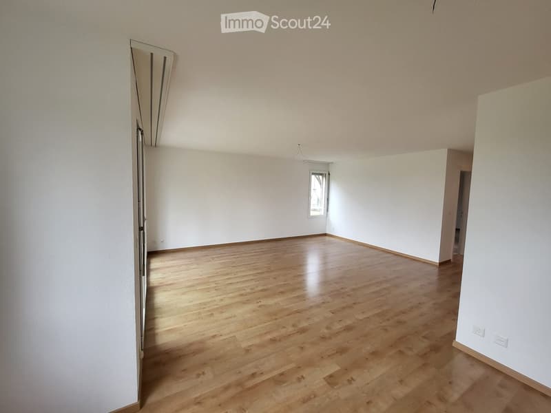 Empty room with light wooden flooring and white walls, featuring a window and a partially open door leading to another space.