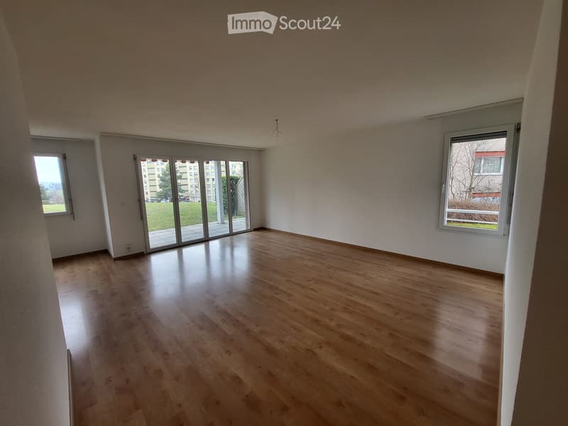 Empty room with wooden flooring, large windows, and sliding glass doors leading to a balcony.