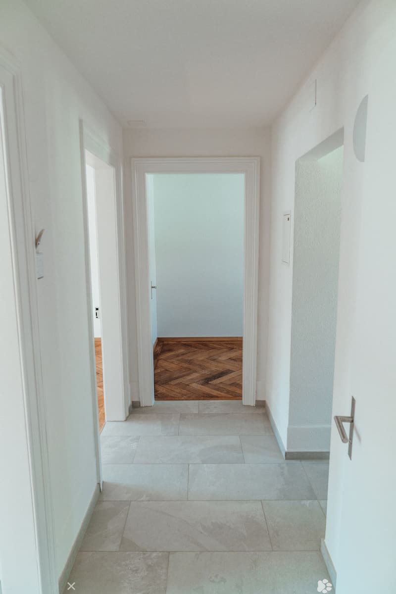 Hallway with white walls, gray flooring, and a wooden floor in the center