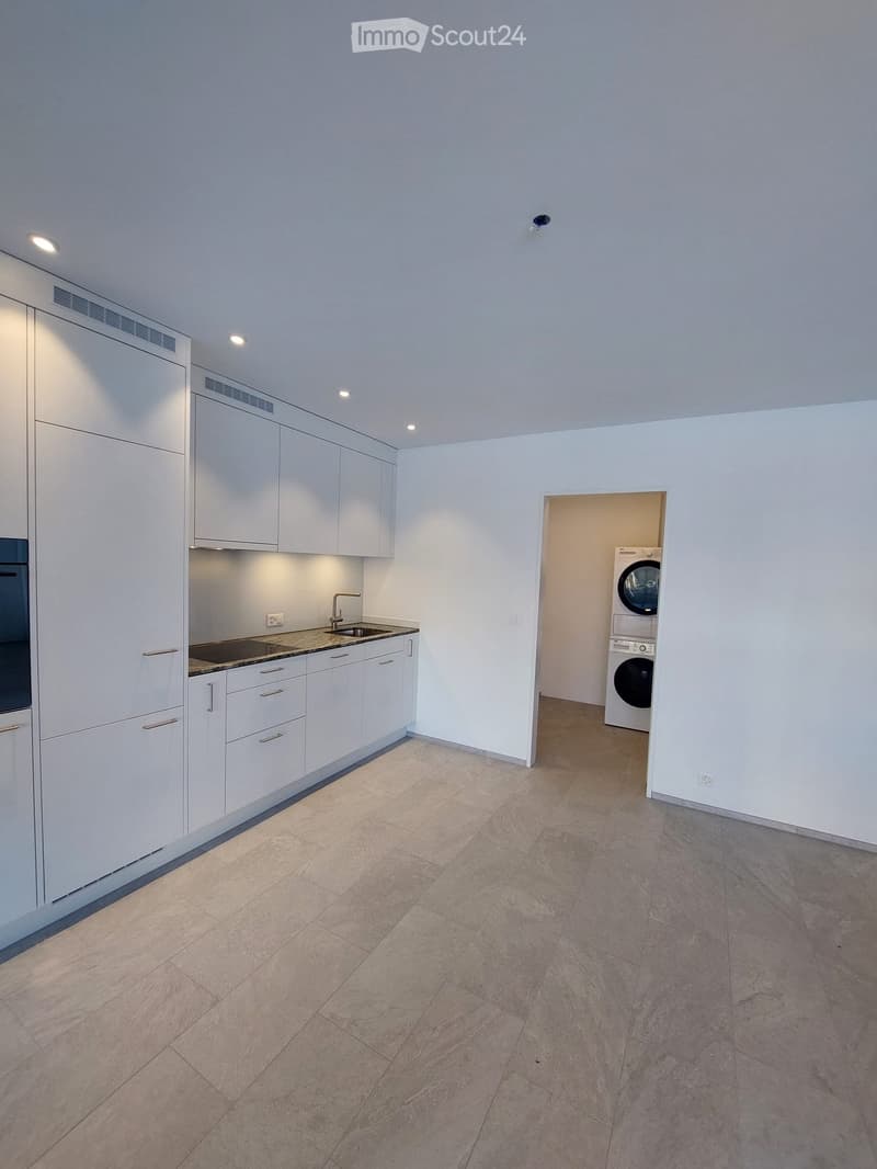 Empty room with white cabinets, sink, and a doorway leading to a private washing machine area.