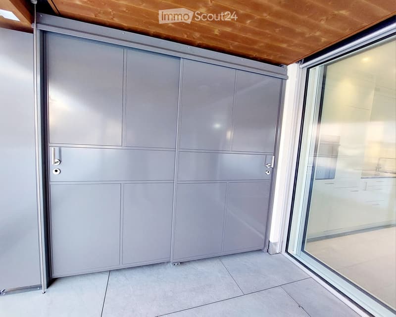 Empty room with grey sliding doors, tiled floor, and large glass window leading to another space.