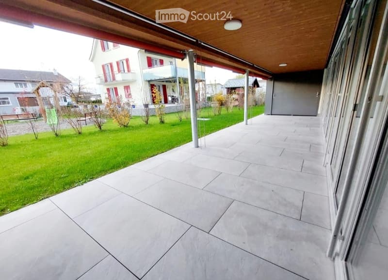 Spacious balcony with wooden ceiling, tiled floor, and open views of a green lawn and neighboring houses.