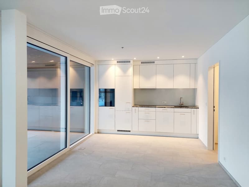 Empty kitchen with white cabinets, a sink, and large glass windows, featuring a tiled floor and recessed lighting.