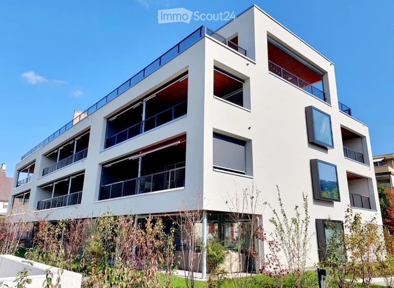 Modern multi-story building with white facade, large windows, and balconies.