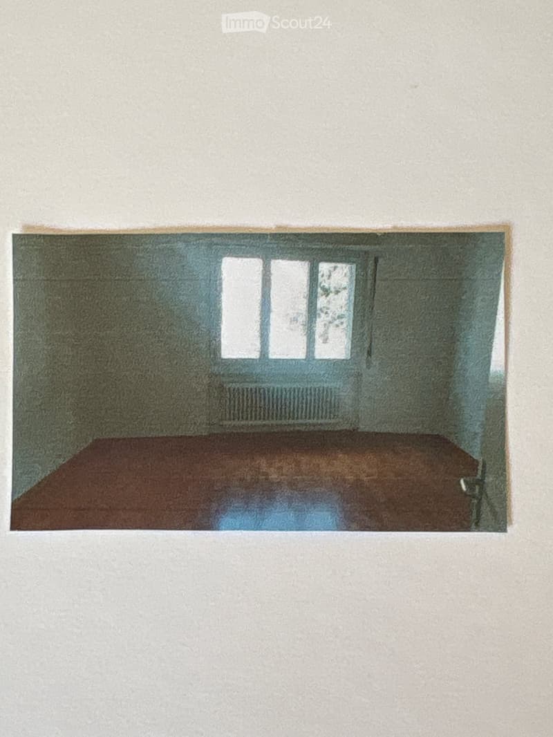 Empty room with bare walls and wooden floor, featuring three windows and a door.
