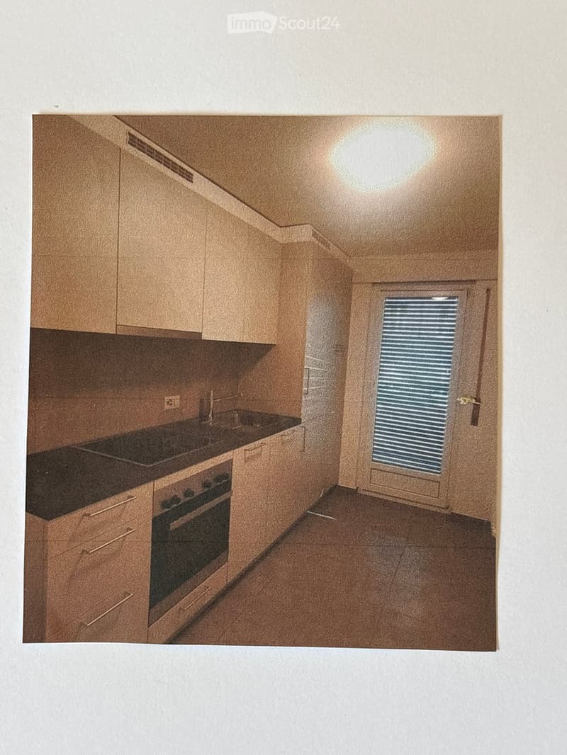 Compact kitchen with light wood cabinets, a black countertop, and an integrated oven. Features a small window with blinds and a sleek, modern design.