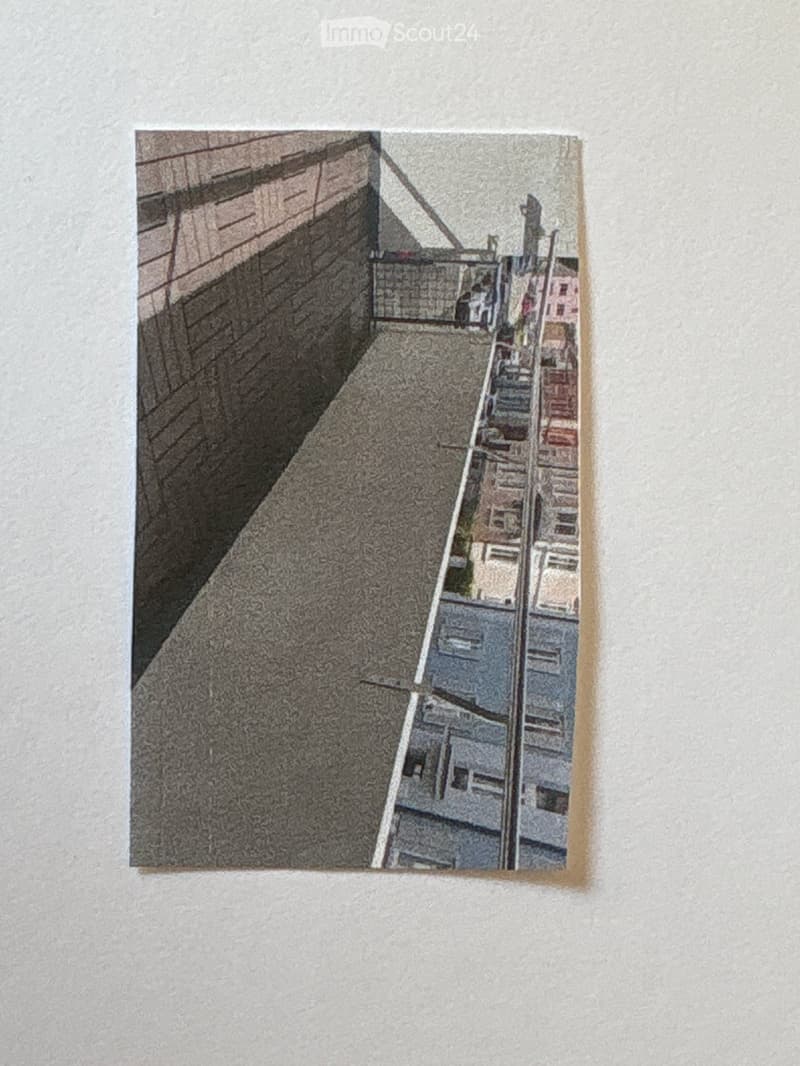 A narrow balcony or terrace with a concrete floor, brick wall on one side, and a view of rooftops and buildings in the distance.