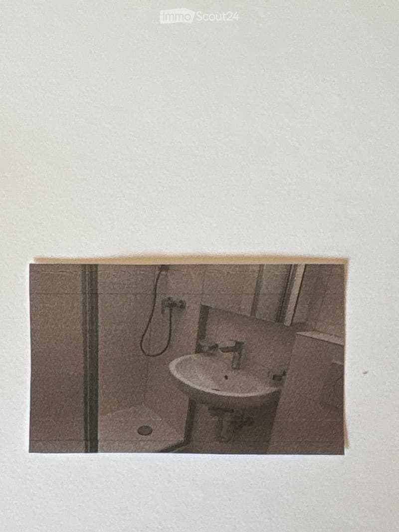 A small bathroom with a sink, faucet, and toilet. The walls are tiled, and the floor appears to be made of concrete or a similar material.