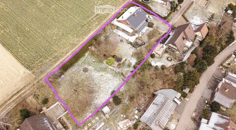Aerial view of a residential area with a highlighted plot of land surrounded by neighboring houses and a field.