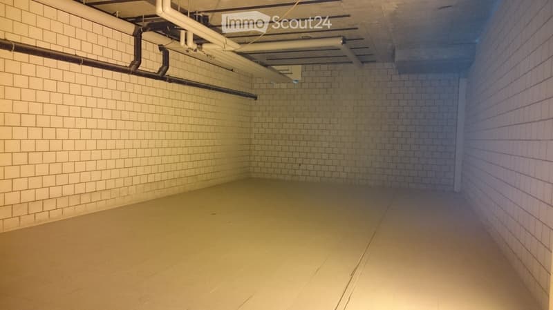 Empty room with white tiled walls and a smooth concrete floor, featuring exposed pipes and ductwork on the ceiling.