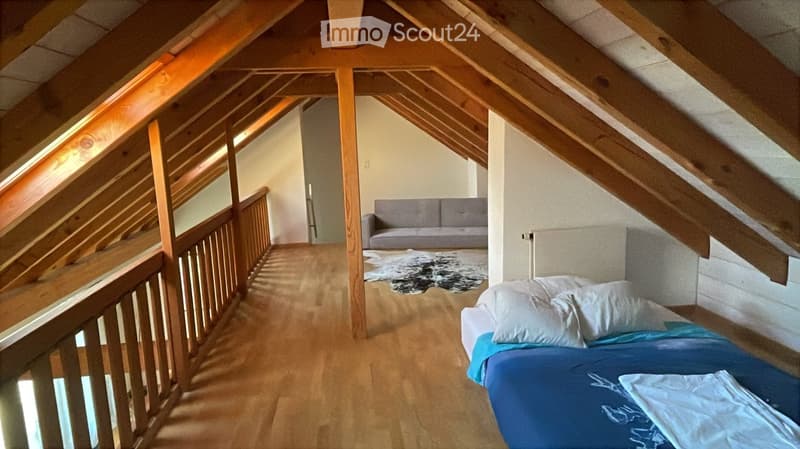 Loft-style bedroom with wooden beams, exposed ceiling, a bed with blue bedding, a sofa, and a fur rug on the floor.
