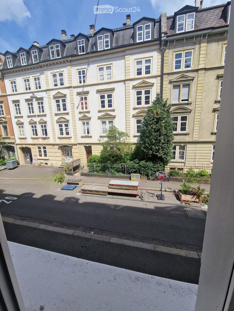 View of a multi-story residential building with classic architecture, multiple windows, and a small courtyard with greenery and outdoor furniture.
