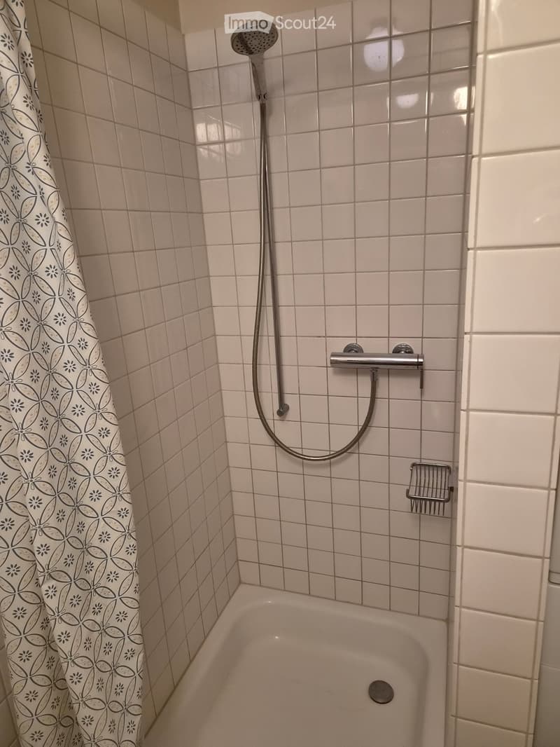 Bathtub with a showerhead and a decorative shower curtain, tiled walls, and a small shower rack.