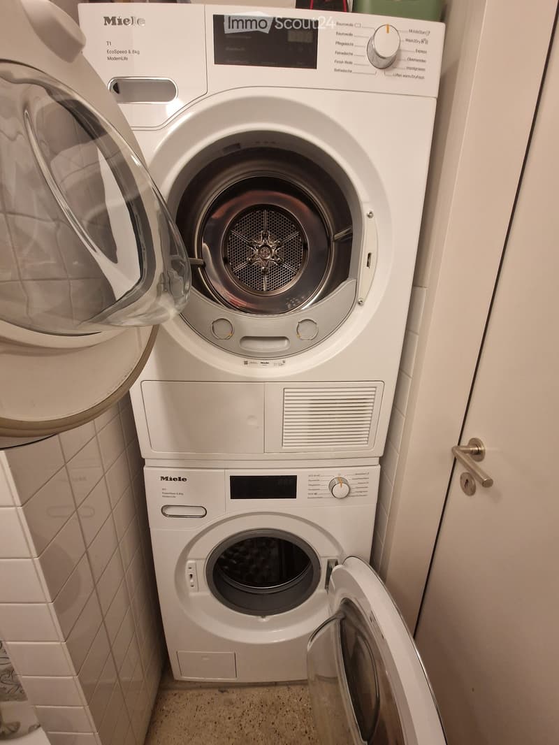 A compact bathroom with a stacked Miele washing machine and dryer unit, both white with control panels and digital displays.