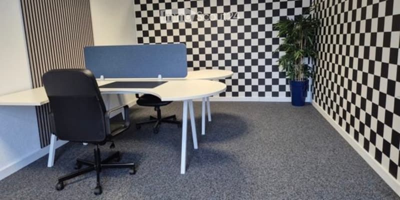 Modern office space with white desks, black office chairs, a computer screen, and a potted plant. The walls feature a black and white checkered pattern.