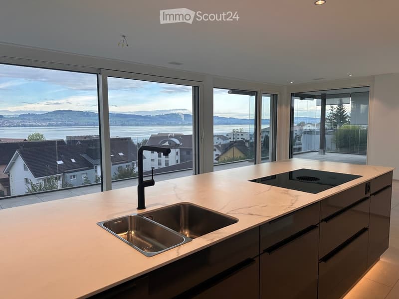 Modern kitchen with a marble countertop, stainless steel sink, black faucet, and induction cooktop, large windows offering a scenic view of the city and water.