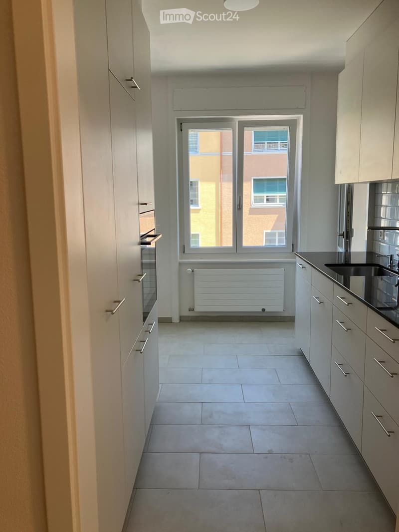 Empty kitchen with white cabinets, tiled floor, and a window with a view of a building.