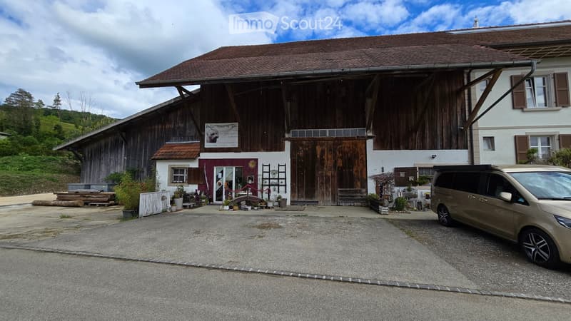 A rustic wooden building with a large barn-like structure, a smaller attached building with a sign, and a parked van in front.