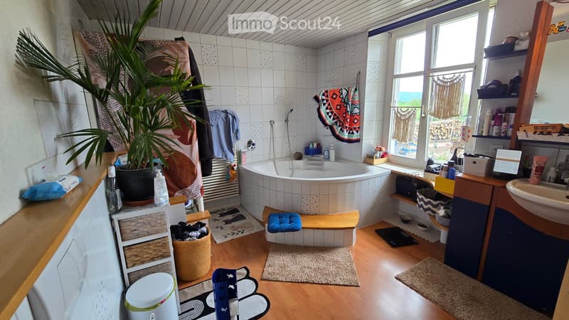 Bathroom with a bathtub, sink, mirror, and shelves. Features a large potted plant, a wooden bench, and various towels and rugs.