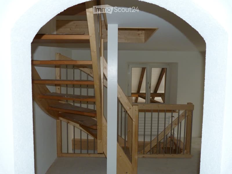 Wooden spiral staircase in the center of the house, wooden handrail, landing with windows