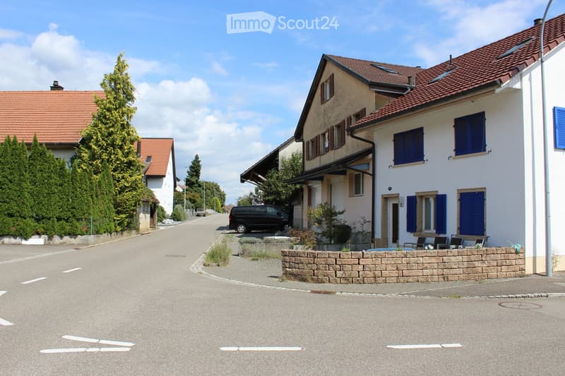 a street with row of houses on the right, a black van is parked outside the houses, street is empty, trees in front of the houses