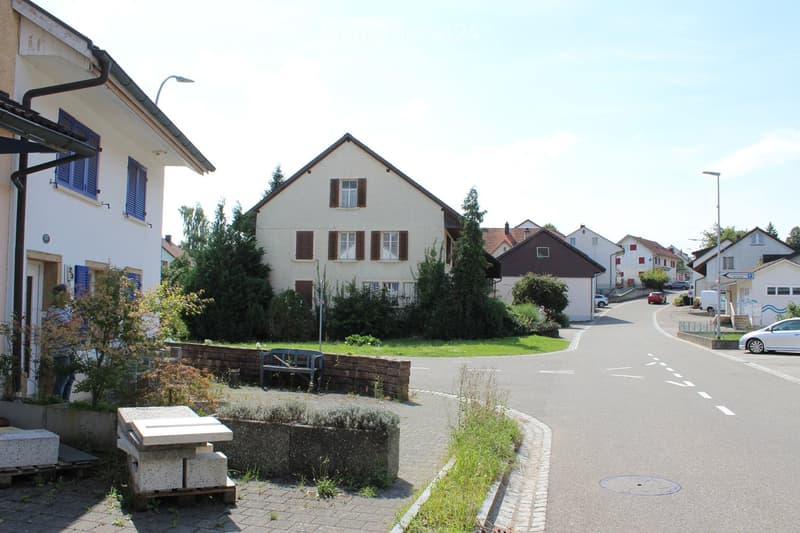 row of houses, white houses with brown shutters, green lawn in front, brick road, cars driving on road