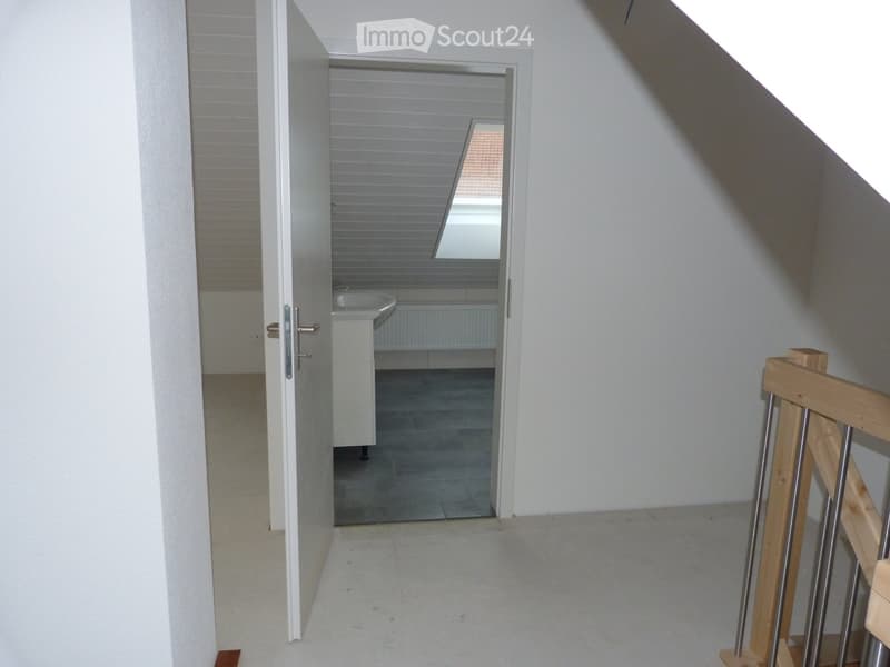 White walls, wooden floor, open door leading to a bathroom with sink and window, wooden staircase