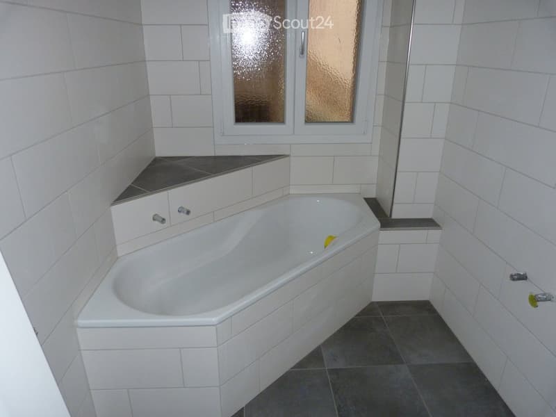 Bathroom with white tiles, corner bathtub, window with frosted glass.