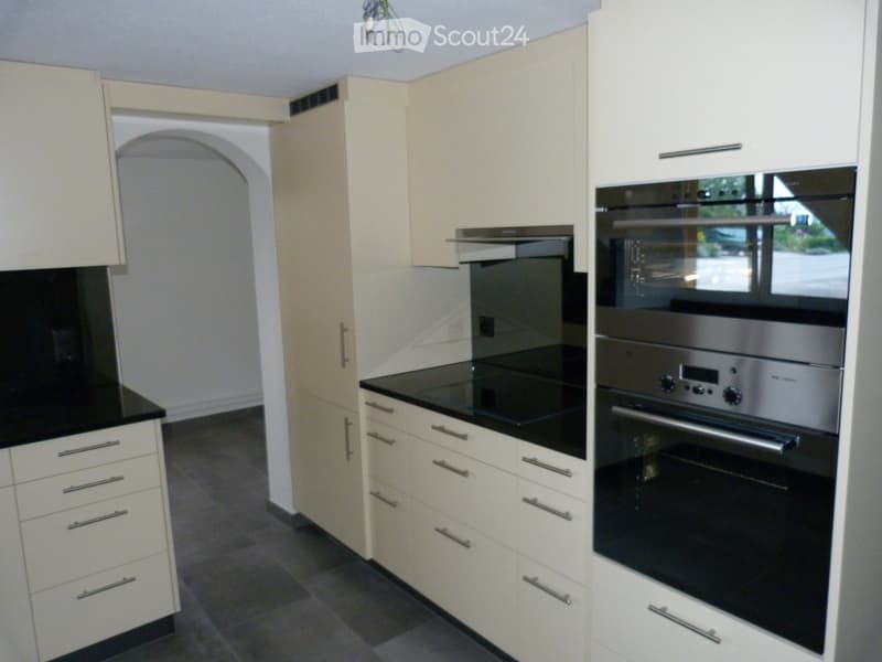 modern kitchen with stainless steel oven and dishwasher, large black worktop, white kitchen units, grey tiled floor