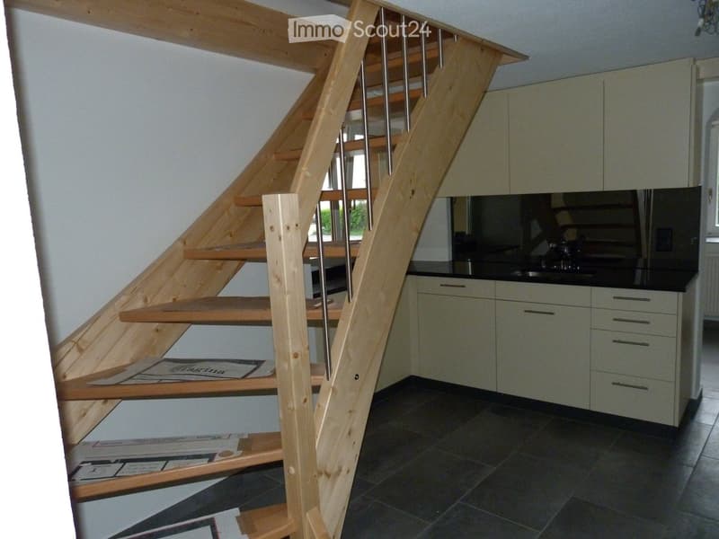 Wooden staircase, white cabinets, black countertops, grey tile flooring, sink