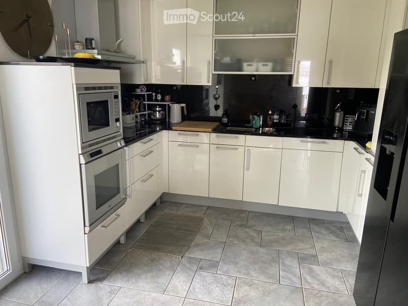 Modern kitchen with white cabinets, stainless steel appliances, and a black countertop. Features include a microwave, oven, refrigerator, sink, and various kitchen items on the counter.