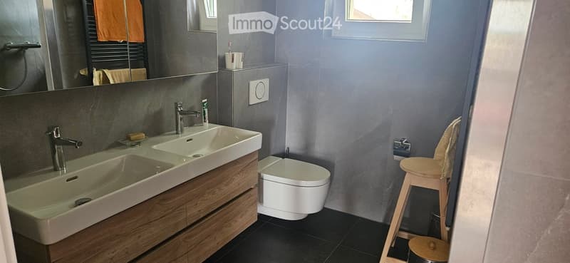 Modern bathroom with double sink, wooden cabinet, toilet, and a small wooden stool with a towel.
