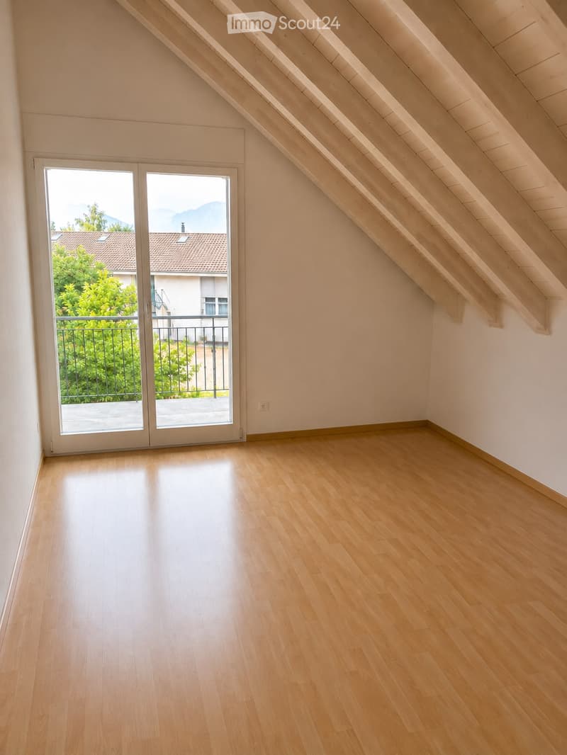 Empty attic room with wooden flooring, large skylight windows, and a sliding glass door leading to a balcony with a view of the surrounding area.
