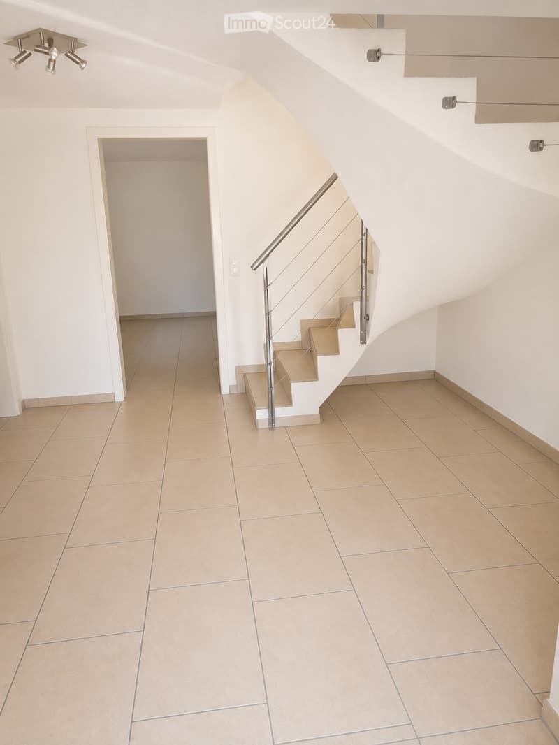 Modern hallway with tiled flooring, white walls, and a staircase with a metal railing leading upwards.