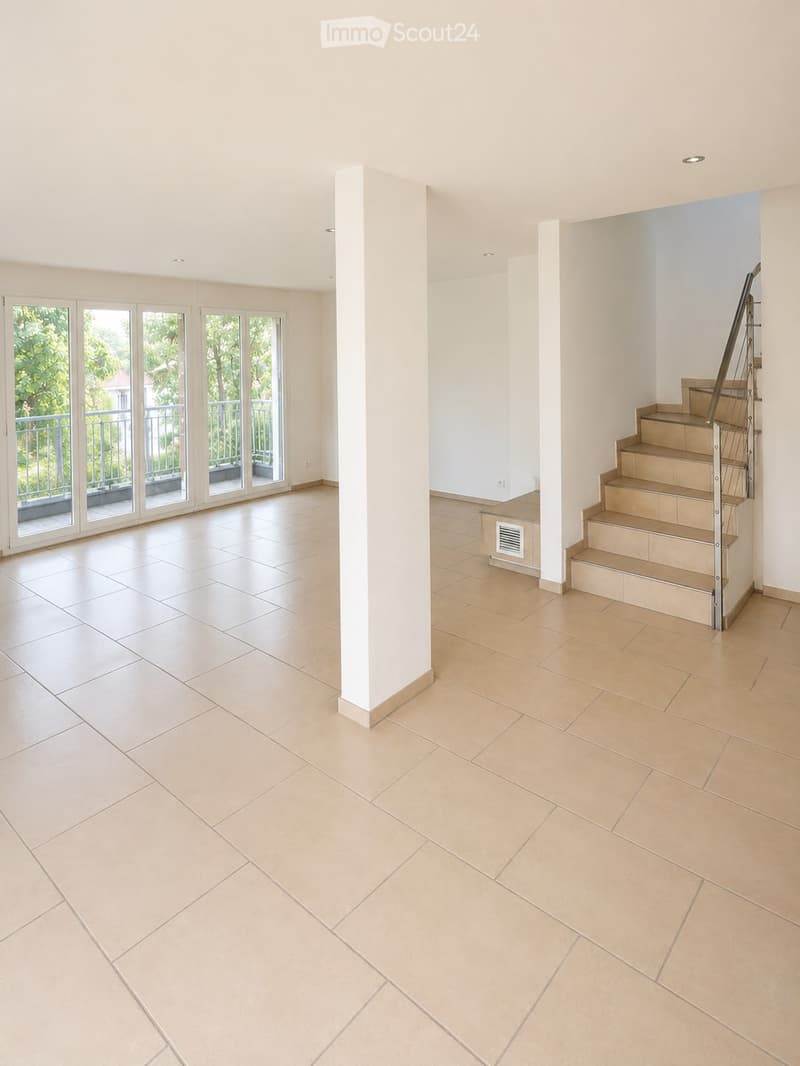 Empty room with beige tiled flooring, white walls, and a staircase leading upwards. Large glass doors open to a balcony area with outdoor views.