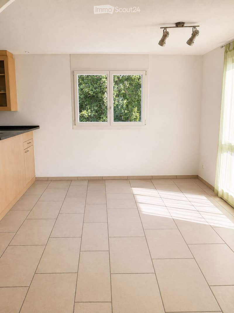 Empty room with tiled floor, white walls, and a window with double panes. There is a small wooden cabinet on the left side and a curtain on the right side.