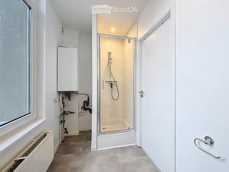 Modern bathroom with a glass-enclosed shower stall, a radiator, and a thermostat unit visible on the wall.