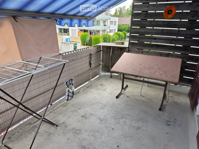 Balcony with a table, chair, laundry rack, and a wooden fence.