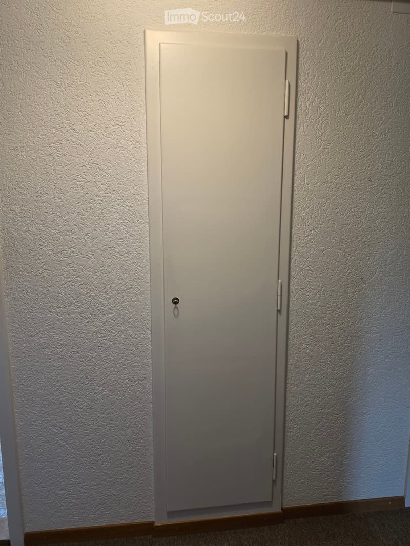 A closed white door with a silver handle and lock, set in a textured wall with a wooden baseboard.