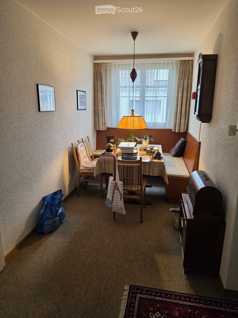 Cozy room with a small table and chairs, a hanging lamp, a built-in sofa, and decorative items including picture frames and a plant.