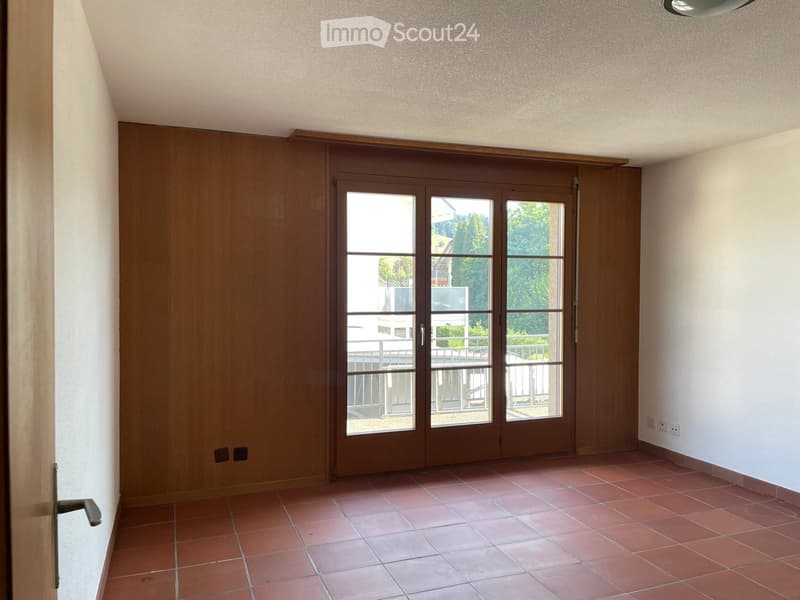 Empty room with tiled floor, large sliding glass door leading to a balcony, and white walls.