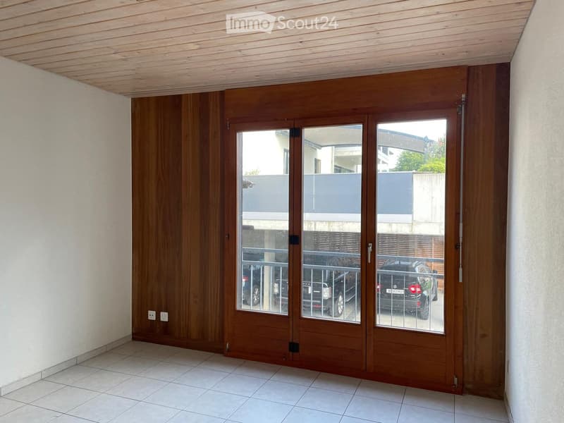 A modern hallway with a large wooden sliding door leading to an outdoor area, tiled floor, and visible electrical outlets on the wall.