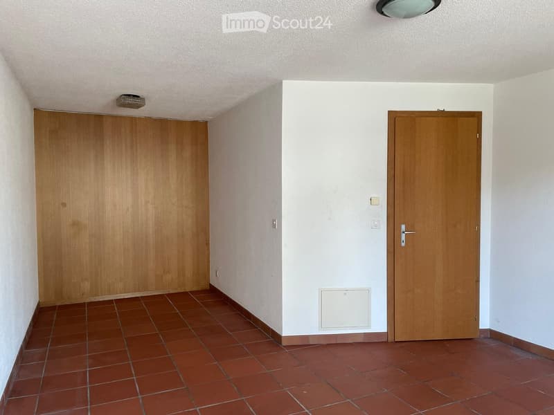 Empty hallway with tiled floor, white walls, two wooden doors, and recessed lighting.