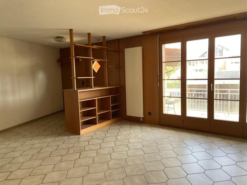 Empty room with hexagonal tiled floor, wooden shelving unit, and large sliding glass doors leading to a balcony.