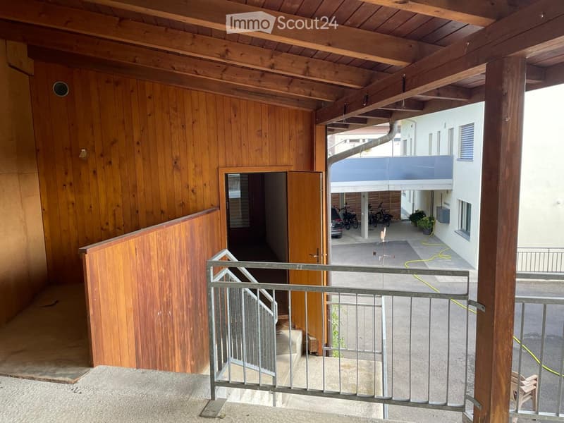 Balcony with wooden walls, metal railing, and access to a covered outdoor area with bicycles and a small garden.