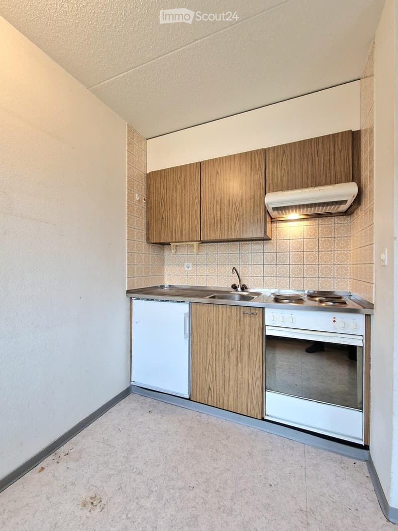 Compact kitchen with wooden cabinets, a refrigerator, an oven, and a sink, featuring tiled walls and a tiled floor.