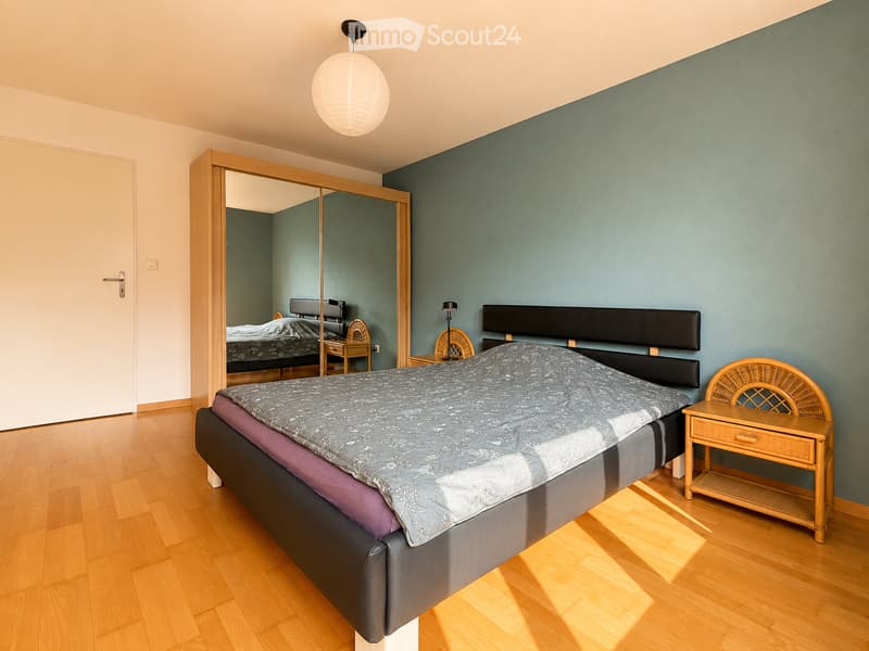 Modern bedroom with a large bed, nightstand, mirror, and a hanging spherical light fixture.