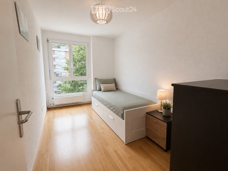 Cozy bedroom with a single bed, nightstand, lamp, potted plant, and drawer unit. The room features light wooden flooring and white walls, with a window offering a view of greenery.