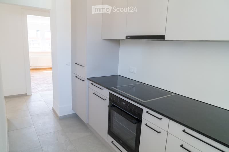 Modern kitchen with white cabinets, black countertops, an induction stove, and an oven. The space is bright and clean with tiled flooring.